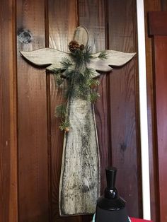 a wooden angel with pine cones on it's back and wings hanging from the wall