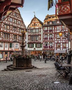 an old town square with people walking around and sitting on benches in front of buildings