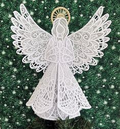 an angel made out of white crochet on top of a green plant in front of a wall