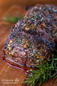 a piece of meat sitting on top of a wooden cutting board next to a sprig of rosemary