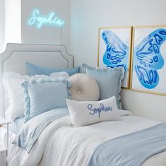 a bed with blue and white pillows in a bedroom next to two framed pictures on the wall