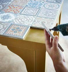 a person is using a pair of scissors to cut out tiles on a table top