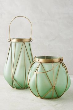 two green vases sitting on top of a white table next to each other with gold handles