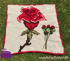 a crocheted blanket with a red rose on it and two roses in the middle