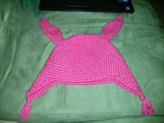 a pink knitted hat sitting on top of a bed next to a laptop computer