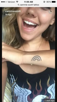 a woman with a tattoo on her arm smiling at the camera and holding onto her wrist