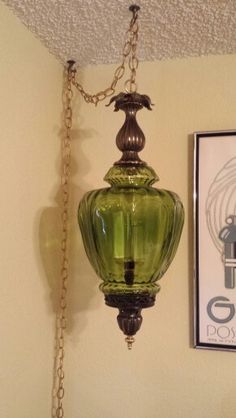 a green lamp hanging from the ceiling next to a framed poster and an old - fashioned light fixture