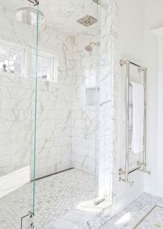 a bathroom with white marble walls and flooring, shower head, and glass door