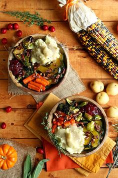 two bowls filled with mashed potatoes, carrots and other vegetables next to corn on the cob