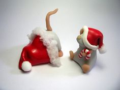 two toy figurines sitting next to each other on a white surface, one is wearing a santa hat and the other has a candy cane in its mouth