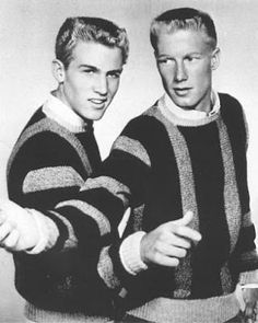 two young men standing next to each other wearing sweaters and pointing fingers at the camera