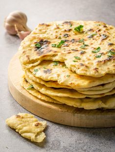 a stack of flat bread sitting on top of a wooden cutting board next to garlic