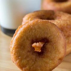 two donuts are on a table with a glass of milk in the background and one is half eaten