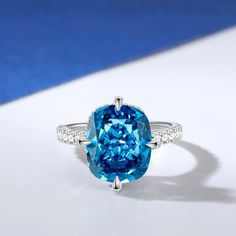 This is a stunning blue stone ring that exudes elegance and sophistication. The centre of the ring is set with a large, captivating blue stone that commands attention with its deep, enchanting hue. The sparkling centre stone is also set with a hidden halo of smaller round stones, and the glittering stone-set band adds to the brilliance of this chic ring. The smooth and delicate design ensures a comfortable fit while showcasing the beauty of the central blue stone.Carat Weight: 6.29 ctStone Size: 10*12 mmStone Type: Jeulia® StoneNumber of Stones: 1 Stone Color: Aquamarine BlueStone Shape: Fat OblongCarat Weight: 1.381 ctStone Size: 1,1.2,1.7,0.8 mmStone Type: Jeulia® StoneNumber of Stones: 68 Stone Color: Diamond WhiteStone Shape: RoundWeight: 2.9 gWidth: 1.9 mmHeight: 10 mmThickness: 1.5 m Chic Rings, Blue Stone Ring, Hidden Halo, Delicate Design, Stone Settings, Cushion Cut, Blue Stone, Stone Ring, Quality Jewelry