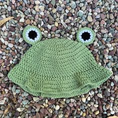 a crocheted frog hat laying on some rocks