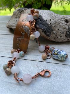 a bracelet with beads and charms sitting on top of a wooden table next to a tree