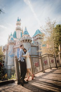 a man and woman standing next to each other in front of a castle at disneyland