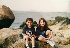 two young children sitting on rocks near the ocean, posing for a photo with their hands in their pockets