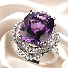 a large purple stone surrounded by diamonds on top of a white satin background with a ring in the middle