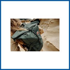 a woman wearing a green backpack in the middle of some sand dunes with her hair blowing back