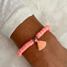 a person wearing a pink and orange bracelet with tassels on their wrist,