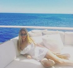 a woman laying on top of a white couch next to the ocean