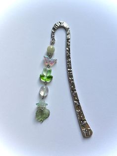 a long silver necklace with green and white beads on it's end, hanging from a chain