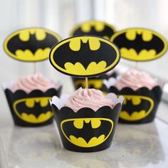 some cupcakes with pink frosting and batman logos on them are sitting on a table