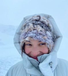 a woman wearing a white jacket and a gray hat in the snow with her mouth open