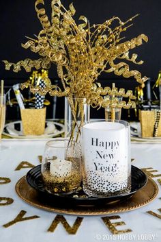 a table topped with glasses and vases filled with gold foiled branches in front of a black background