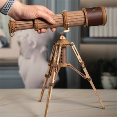 a person holding a wooden telescope on top of a table next to a book shelf