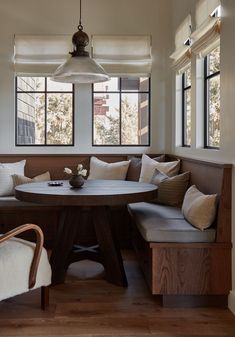 a corner table and bench in a living room with two windows above the couches