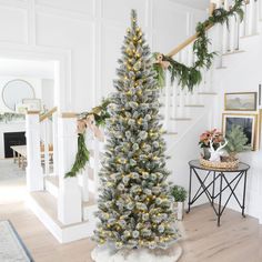 a decorated christmas tree in the corner of a room with stairs and pictures on the wall