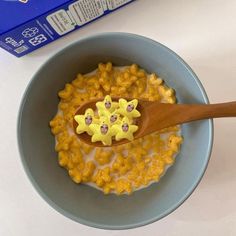 a bowl with cereal in it next to a carton of milk and a wooden spoon