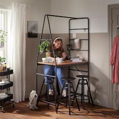 a woman sitting at a desk in front of a potted plant on top of a shelf