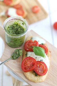 an open face sandwich with tomatoes and pesto on it next to a jar of pesto