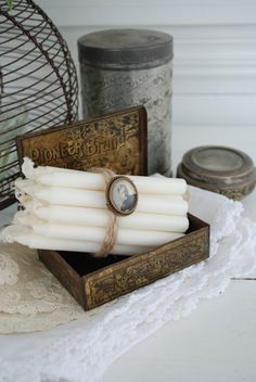 some white candles in a wooden box on a table next to an old tin can