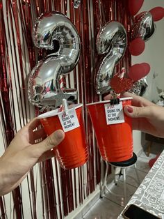 two people holding up red cups with the number 3 on them in front of balloons and streamers