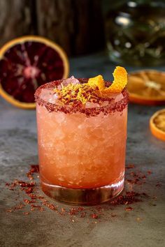 a close up of a drink on a table with oranges and other fruit in the background