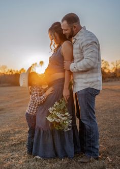 a man and woman standing next to each other in a field with the sun setting behind them