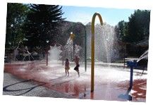 two children playing in a water park with sprinkles on the ground and trees behind them