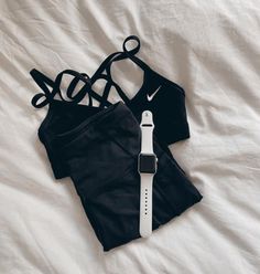 an apple watch and two black sports bras on a bed with white linens