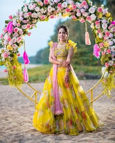 a woman standing in front of a floral arch with flowers on it and wearing a yellow dress