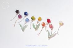 five different colored flowers are in a row on a white surface with the words tulip dangle earring written below them