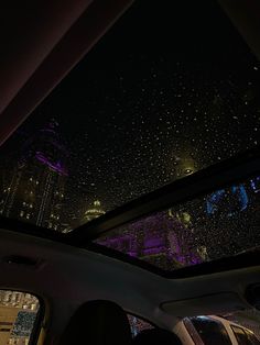 the inside of a car with rain falling on it's windshield and buildings in the background