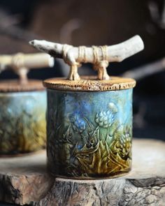 two ceramic pots with handles on top of a piece of wood