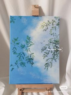 an easel with a painting on it holding a blue sky and green tree branches