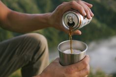 a man is pouring something into a small metal cup with the lid down and his hands are on the ground