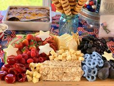 a table topped with crackers, fruit and other foods on top of a red white and blue cloth