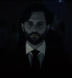 a man in a suit and tie looking at the camera with dark lighting behind him